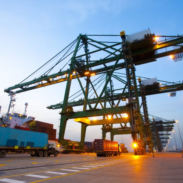 Cranes, cargo containers and trucks at a shipping port during dusk